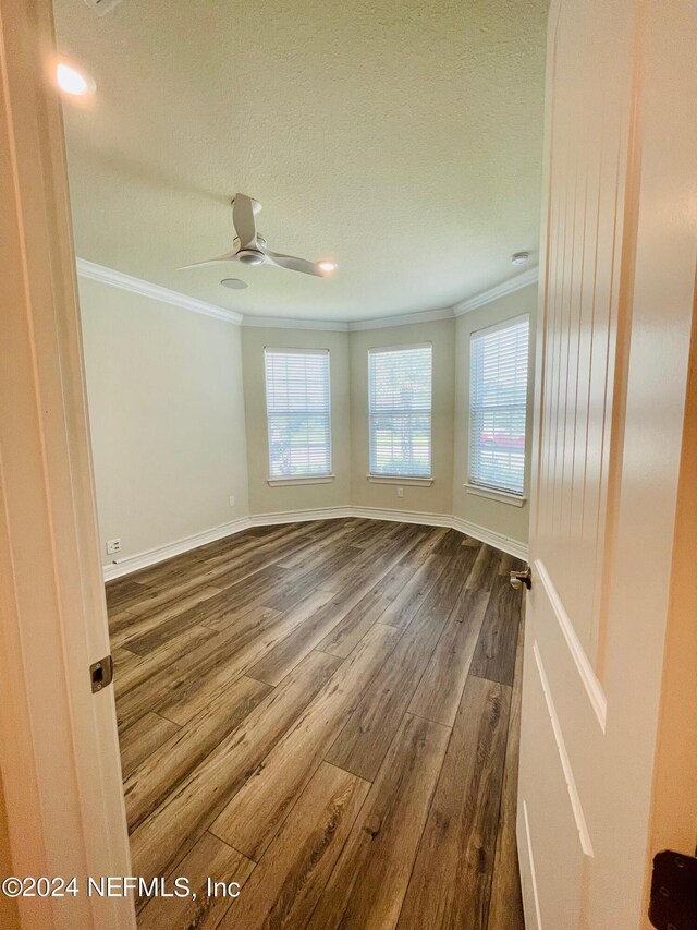 empty room with crown molding, hardwood / wood-style flooring, a textured ceiling, and a healthy amount of sunlight