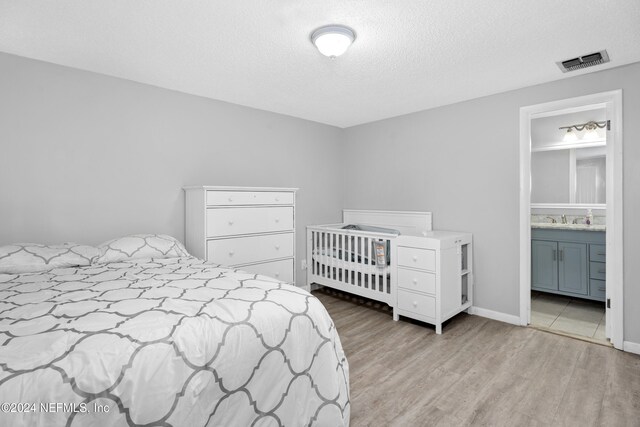 bedroom featuring sink, connected bathroom, a textured ceiling, and light wood-type flooring