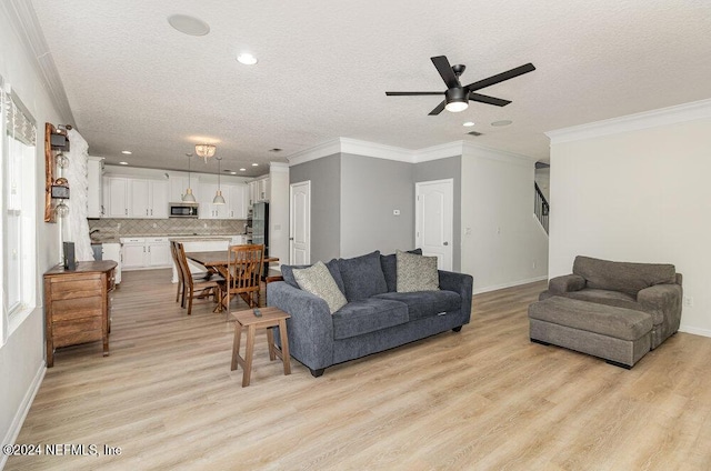 living room featuring ceiling fan, light hardwood / wood-style flooring, ornamental molding, and a textured ceiling