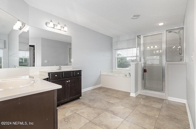 bathroom featuring a textured ceiling, two vanities, baseboards, a bath, and a stall shower