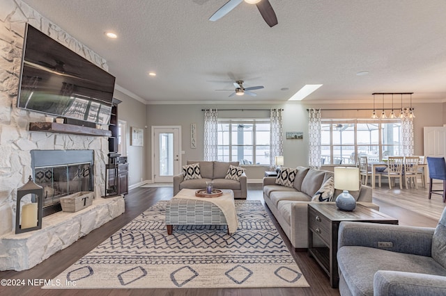 living area with a textured ceiling, ceiling fan, a fireplace, ornamental molding, and dark wood finished floors