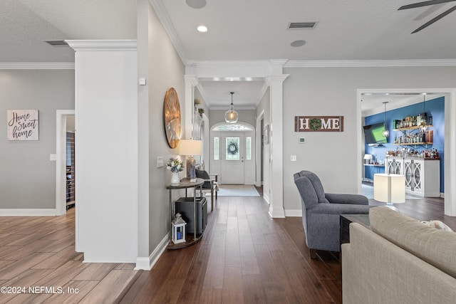 foyer entrance with visible vents, dark wood-style floors, crown molding, a bar, and ornate columns