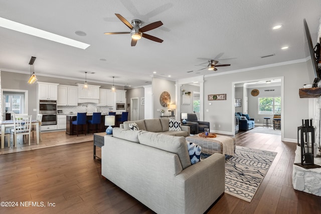 living room with a textured ceiling, ceiling fan, dark wood-type flooring, baseboards, and crown molding