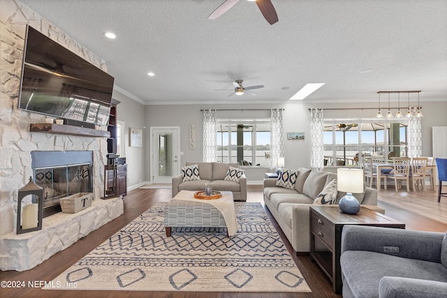 living area with dark wood-style flooring, crown molding, a fireplace, a ceiling fan, and a textured ceiling