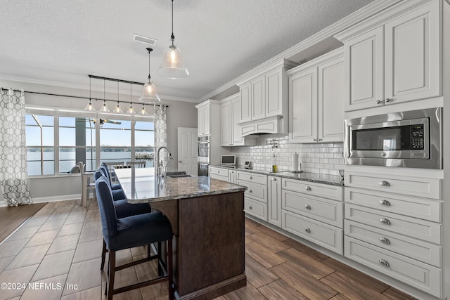 kitchen featuring stone countertops, decorative backsplash, an island with sink, appliances with stainless steel finishes, and a sink