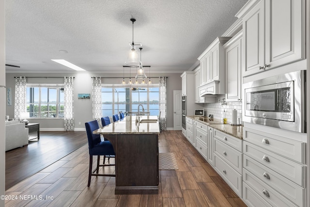 kitchen featuring stainless steel appliances, wood finish floors, white cabinetry, tasteful backsplash, and a kitchen bar