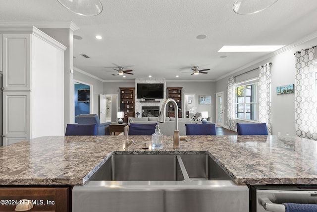 kitchen with crown molding, stone counters, a fireplace, and a sink