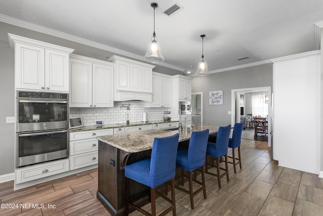 kitchen with double oven, black electric stovetop, visible vents, backsplash, and an island with sink