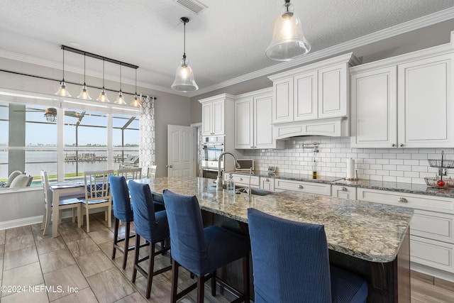 kitchen with visible vents, decorative backsplash, white cabinets, ornamental molding, and a water view