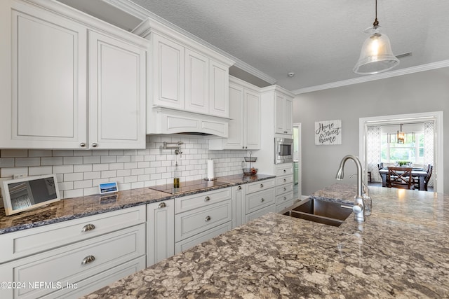 kitchen with decorative backsplash, white cabinets, ornamental molding, black electric stovetop, and a sink