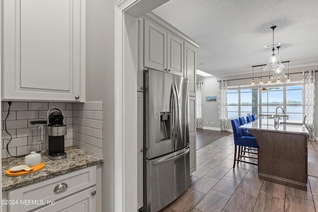 kitchen with stainless steel refrigerator with ice dispenser, tasteful backsplash, a sink, a textured ceiling, and light stone countertops