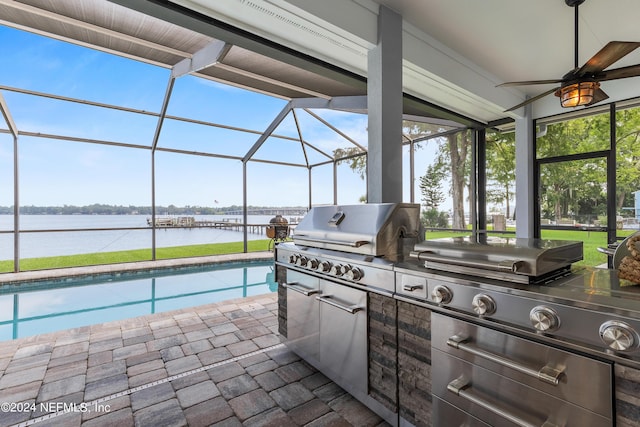 view of patio / terrace featuring a grill, glass enclosure, a water view, and an outdoor kitchen