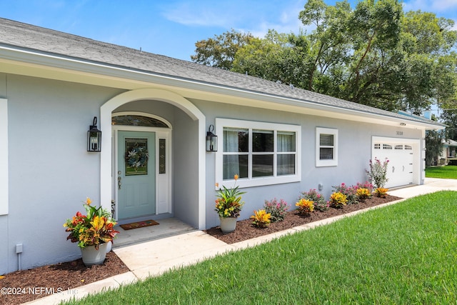 entrance to property with a garage, a shingled roof, and stucco siding