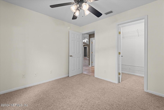 unfurnished bedroom with a closet, light colored carpet, a spacious closet, and ceiling fan