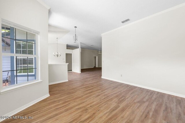 empty room with an inviting chandelier, hardwood / wood-style flooring, lofted ceiling, and ornamental molding