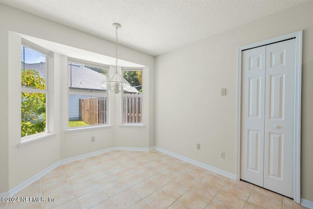 unfurnished dining area with a notable chandelier, plenty of natural light, baseboards, and a textured ceiling