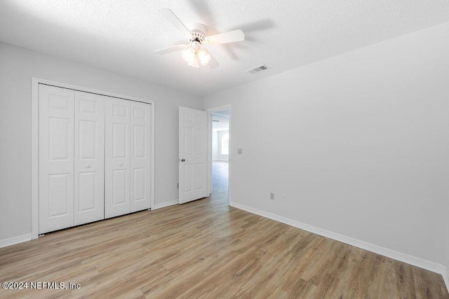 unfurnished bedroom with light wood-type flooring, a textured ceiling, visible vents, and a closet