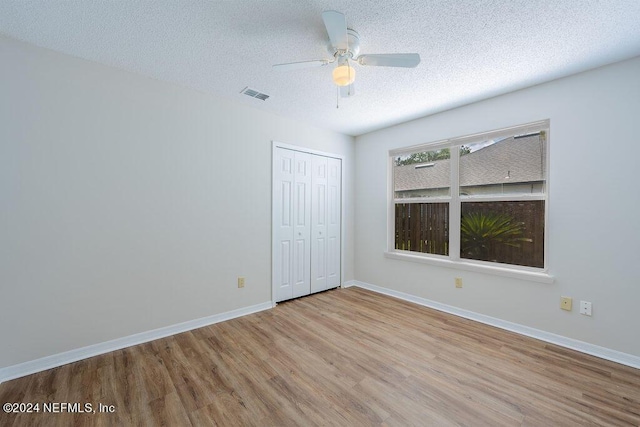 unfurnished bedroom with a closet, visible vents, a textured ceiling, wood finished floors, and baseboards