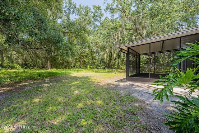 view of yard featuring driveway, a forest view, and a sunroom