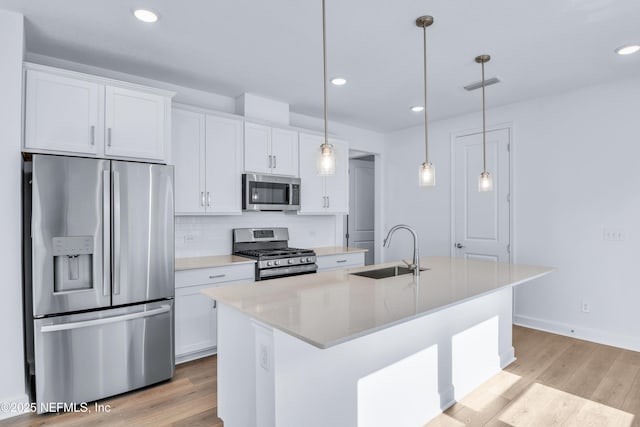 kitchen featuring sink, appliances with stainless steel finishes, hanging light fixtures, white cabinets, and a center island with sink