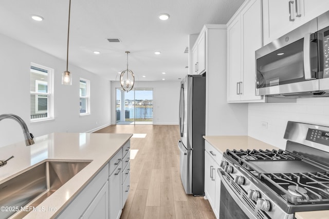 kitchen featuring appliances with stainless steel finishes, pendant lighting, white cabinetry, sink, and decorative backsplash