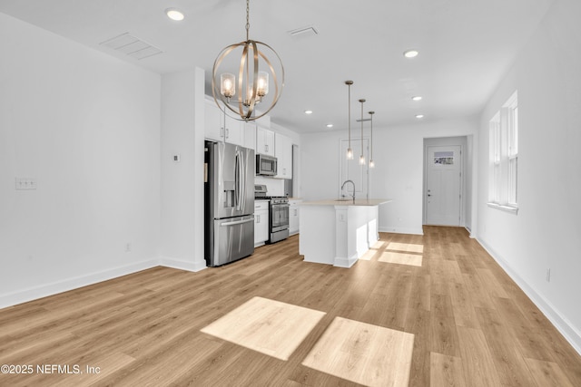 kitchen with white cabinetry, stainless steel appliances, hanging light fixtures, and a center island with sink