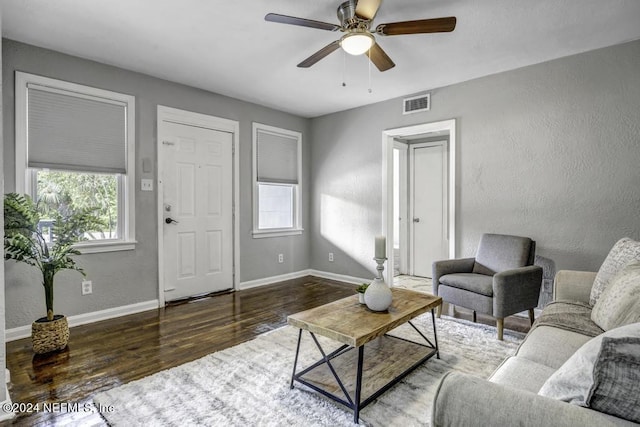 living room with a textured wall, wood finished floors, visible vents, and baseboards