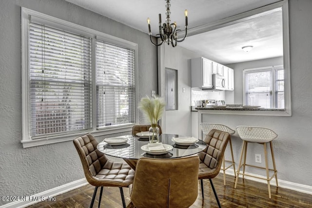 dining area with a notable chandelier, a textured wall, dark wood-type flooring, and baseboards