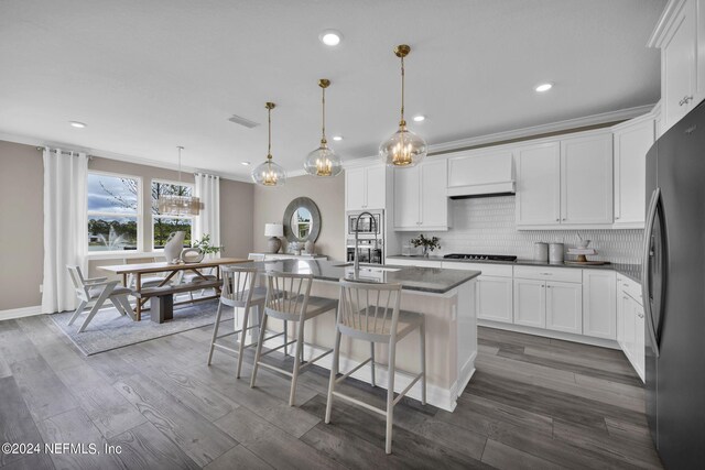 kitchen with dark hardwood / wood-style floors, pendant lighting, tasteful backsplash, a kitchen island with sink, and black refrigerator