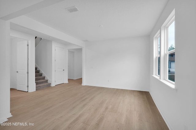 spare room featuring visible vents, baseboards, light wood-style floors, and stairs