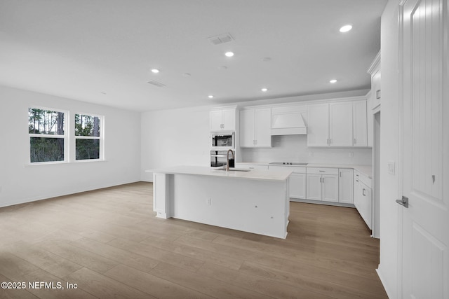 kitchen with built in microwave, light wood-type flooring, black electric cooktop, and a sink