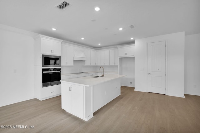 kitchen featuring oven, custom range hood, a sink, stainless steel microwave, and black electric stovetop