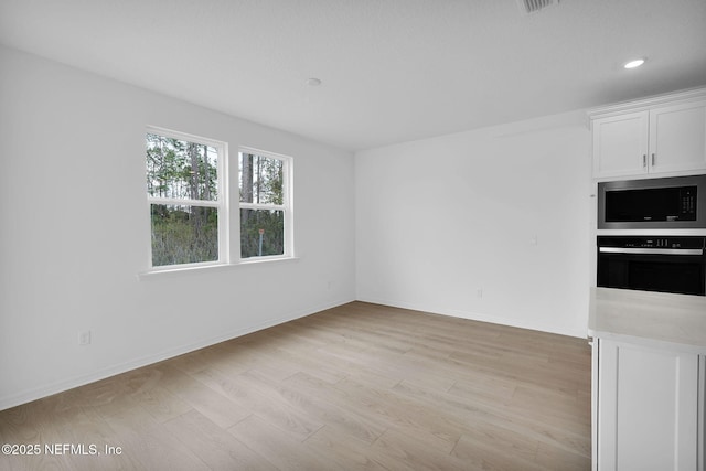 interior space with light countertops, white cabinets, light wood-style floors, stainless steel microwave, and black oven