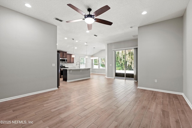 unfurnished living room featuring lofted ceiling, sink, light wood-type flooring, ceiling fan, and a textured ceiling