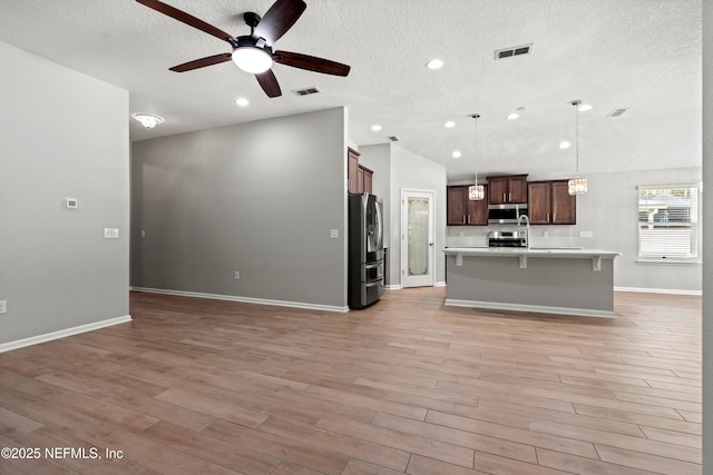 kitchen featuring vaulted ceiling, hanging light fixtures, stainless steel appliances, a center island with sink, and light hardwood / wood-style flooring