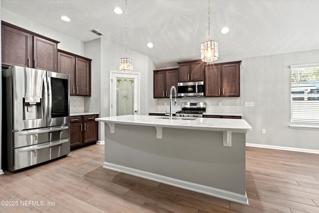 kitchen with pendant lighting, stainless steel appliances, a kitchen island with sink, and sink