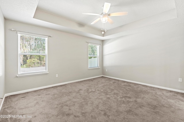 empty room with a textured ceiling, a raised ceiling, ceiling fan, and carpet flooring