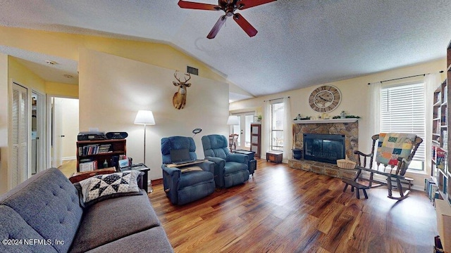 living room with vaulted ceiling, a fireplace, hardwood / wood-style flooring, ceiling fan, and a textured ceiling