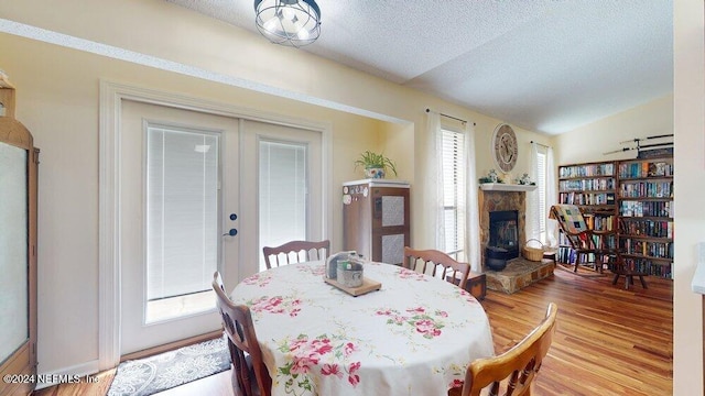 dining space featuring french doors, lofted ceiling, a textured ceiling, a fireplace, and light hardwood / wood-style floors