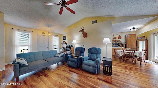 living room featuring ceiling fan, vaulted ceiling, light hardwood / wood-style flooring, and a textured ceiling