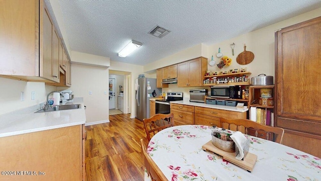 kitchen with appliances with stainless steel finishes, sink, hardwood / wood-style floors, and a textured ceiling