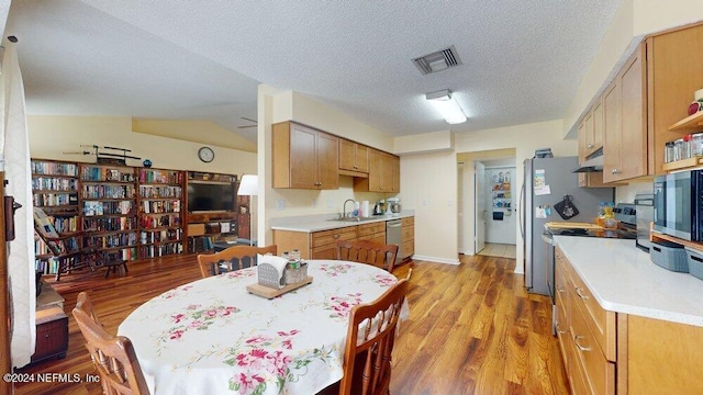 kitchen with vaulted ceiling, sink, light hardwood / wood-style floors, stainless steel appliances, and a textured ceiling