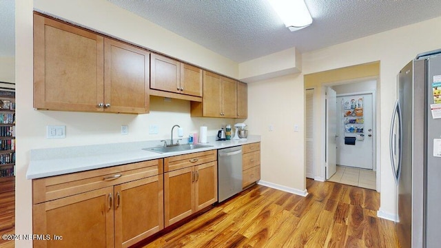 kitchen with stainless steel appliances, sink, a textured ceiling, and light hardwood / wood-style floors