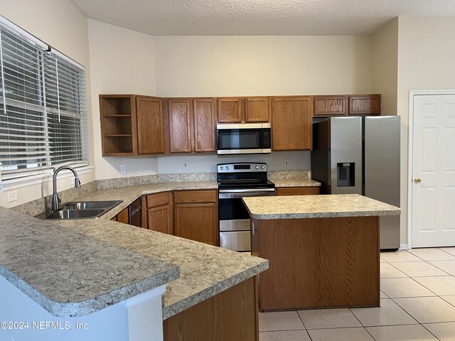 kitchen with light tile patterned floors, kitchen peninsula, a textured ceiling, stainless steel appliances, and sink