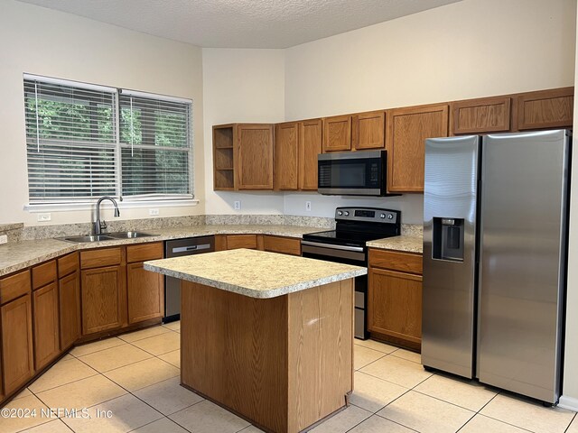 kitchen featuring stainless steel appliances, sink, light tile patterned floors, a kitchen island, and a textured ceiling