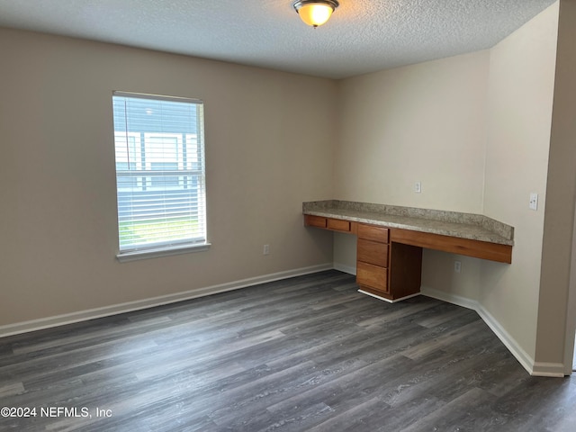 unfurnished office with dark wood-type flooring, built in desk, and a textured ceiling