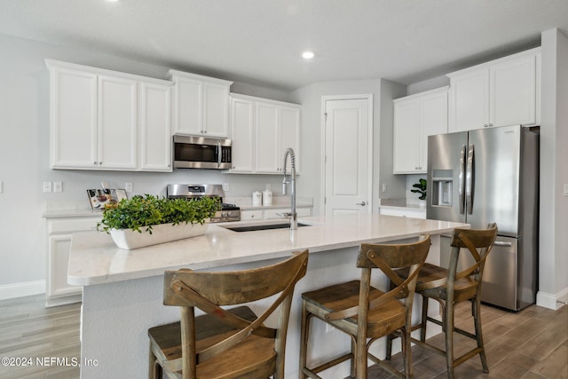 kitchen featuring an island with sink, stainless steel appliances, hardwood / wood-style floors, and white cabinetry