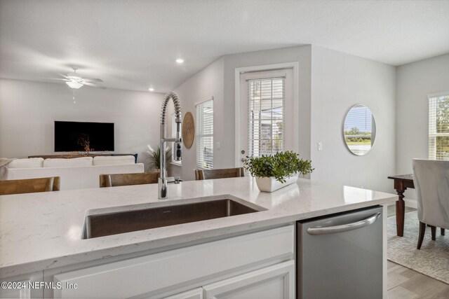 kitchen with light wood-type flooring, dishwasher, light stone counters, ceiling fan, and sink