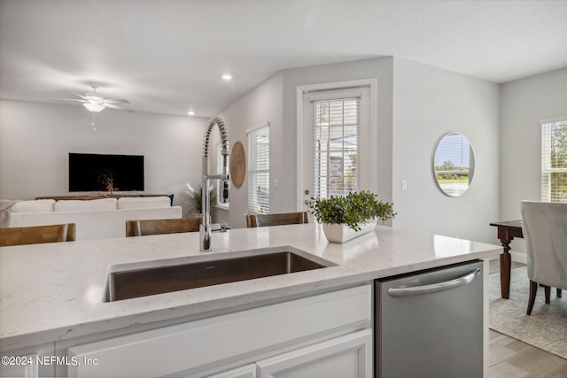 kitchen with sink, light hardwood / wood-style flooring, light stone counters, white cabinets, and stainless steel dishwasher