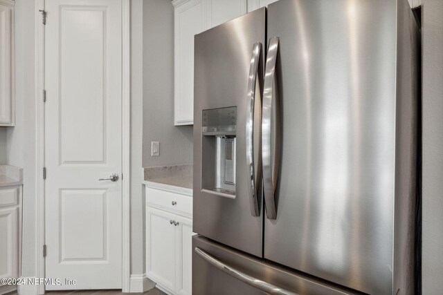 kitchen with light stone counters, white cabinetry, and stainless steel fridge